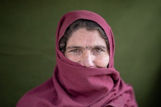 A middle-aged woman in a burgundy hijab stares into the camera.