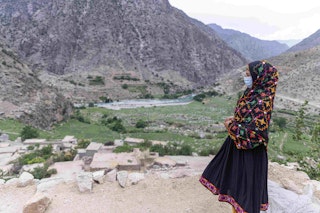 a young woman in a coloured outfit looks out over a fertile valley and mountains.