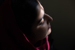 Sunlight shines on the profile of a young woman wearing makeup, looking to the right.
