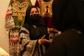 A masked and veiled young woman speaks to customers at a clothing stall