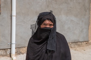 A woman stands, draped in a black lace veil.