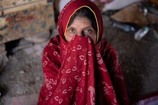 A woman holds her red hijab over her mouth and nose.