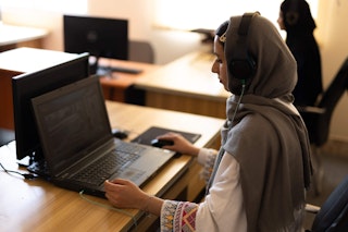 A young woman sits at a desk, typing on her laptop.