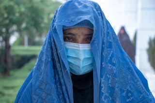 A younger woman in a facemask and blue veil stands outdoors.