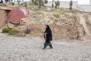A veiled woman holding papers walks down a stone path.