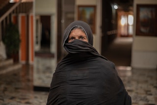 An older woman in a black dress and veil stands in a public building.