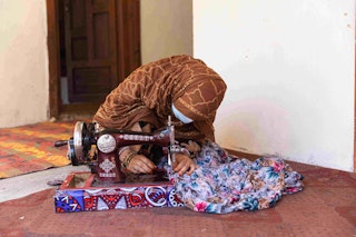 A woman hunches over a sewing machine on the floor.