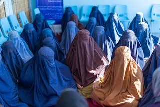 More than a dozen women shrouded in burqas sit in a room.