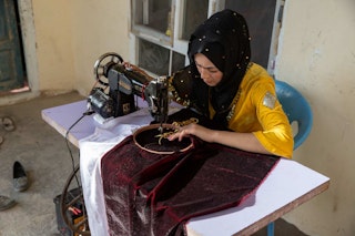 Woman dressed in yellow sews red velvet material at a sewing machine.