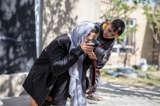 A woman takes photographs through a camera while a boy looks on.