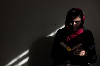 A young woman reads a book in dim light.