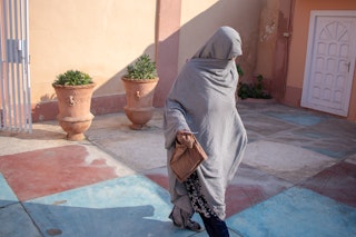 Woman in a hijab walks along a tile courtyard.