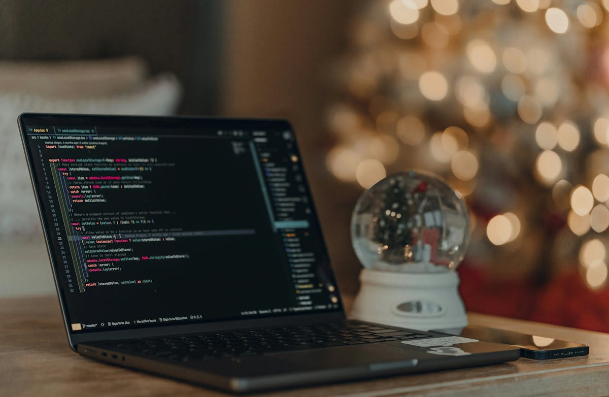 A laptop and snow globe on a table with holiday lights in background