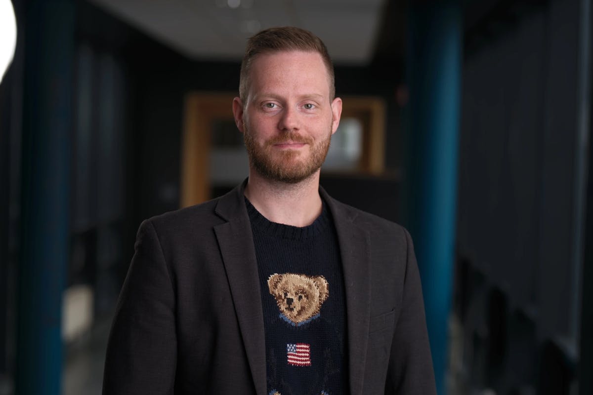 Image of a man in a blazer and a teddy bear t-shirt in an office hallway