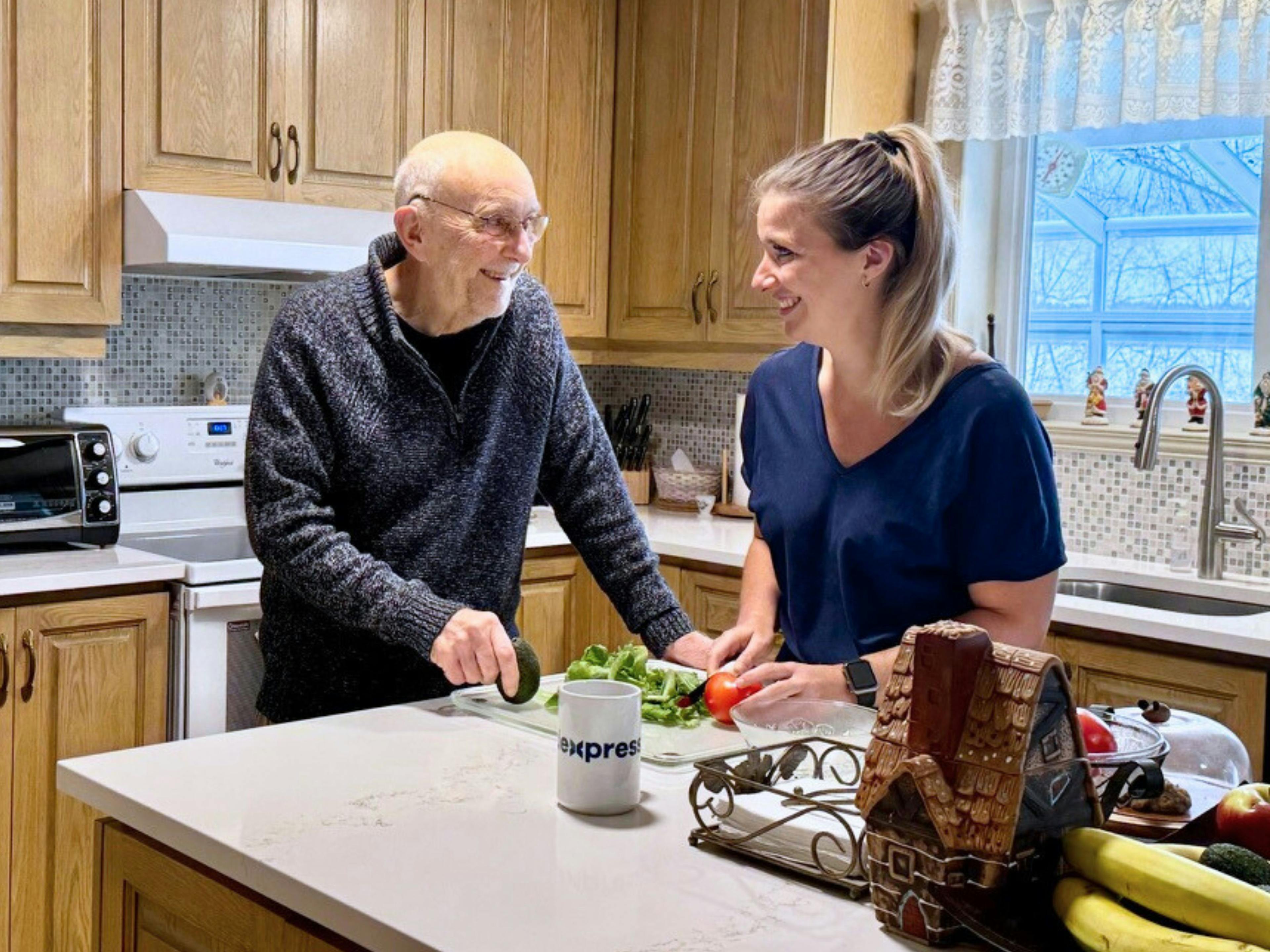 Une aidante souriante qui prépare un repas à une personne âgée à son domicile