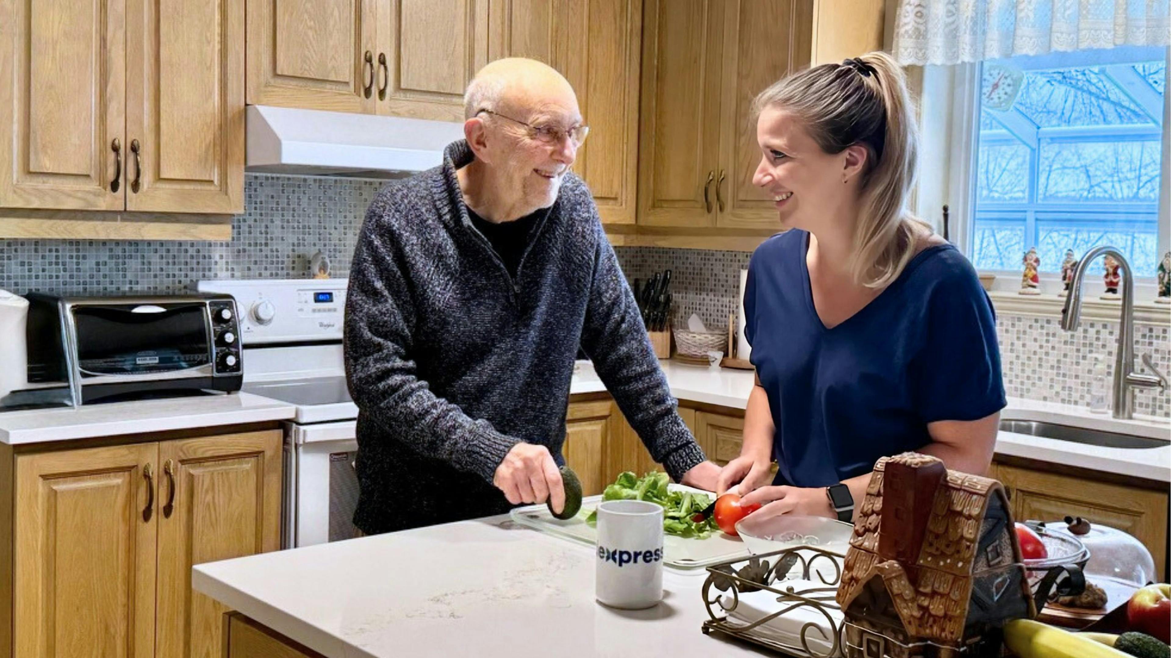 Une aidante souriante qui prépare un repas à une personne âgée à son domicile