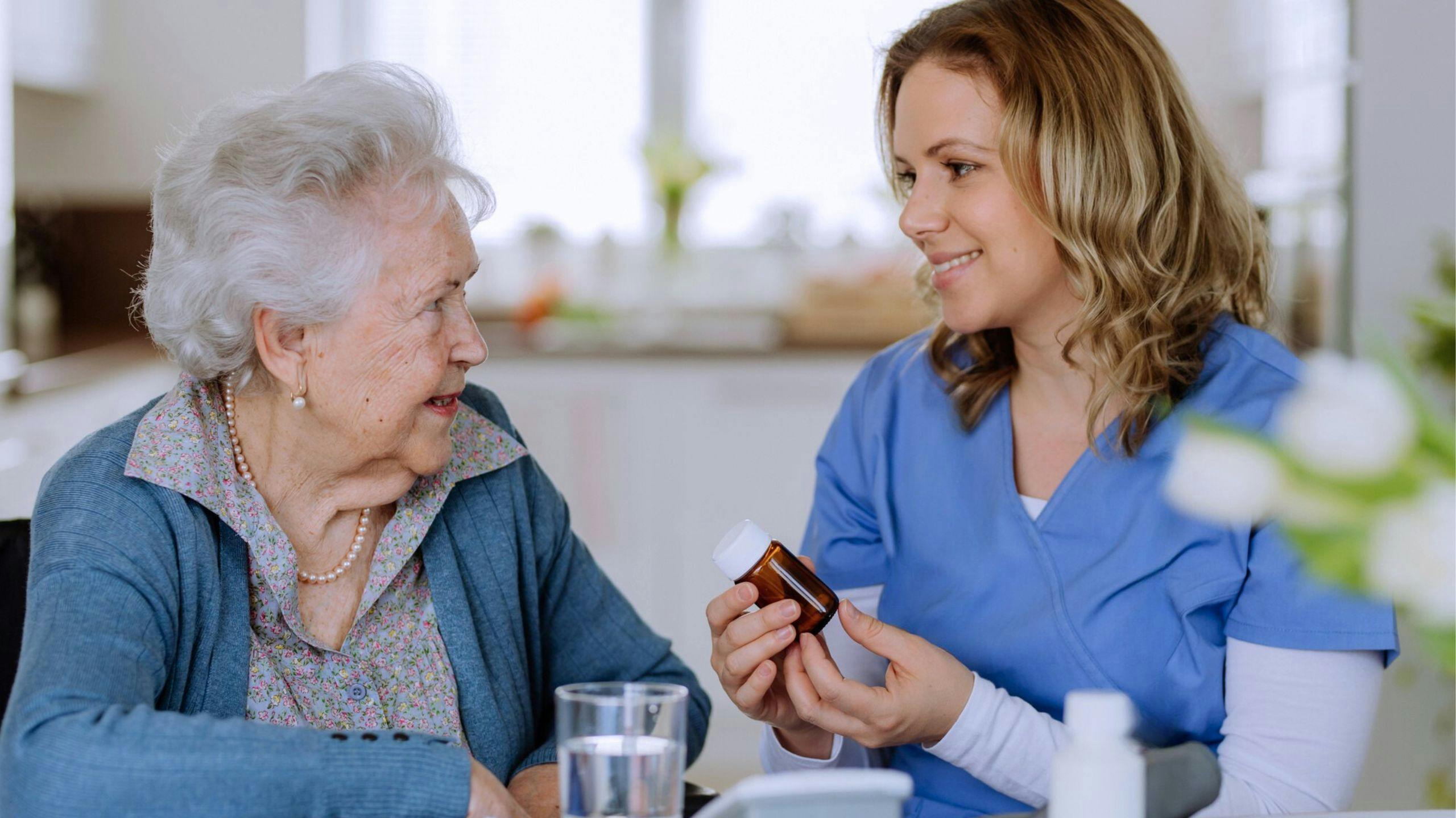 une aidante qui fait un rappel à la personne âgée qu'il est temps de prendre son médicament