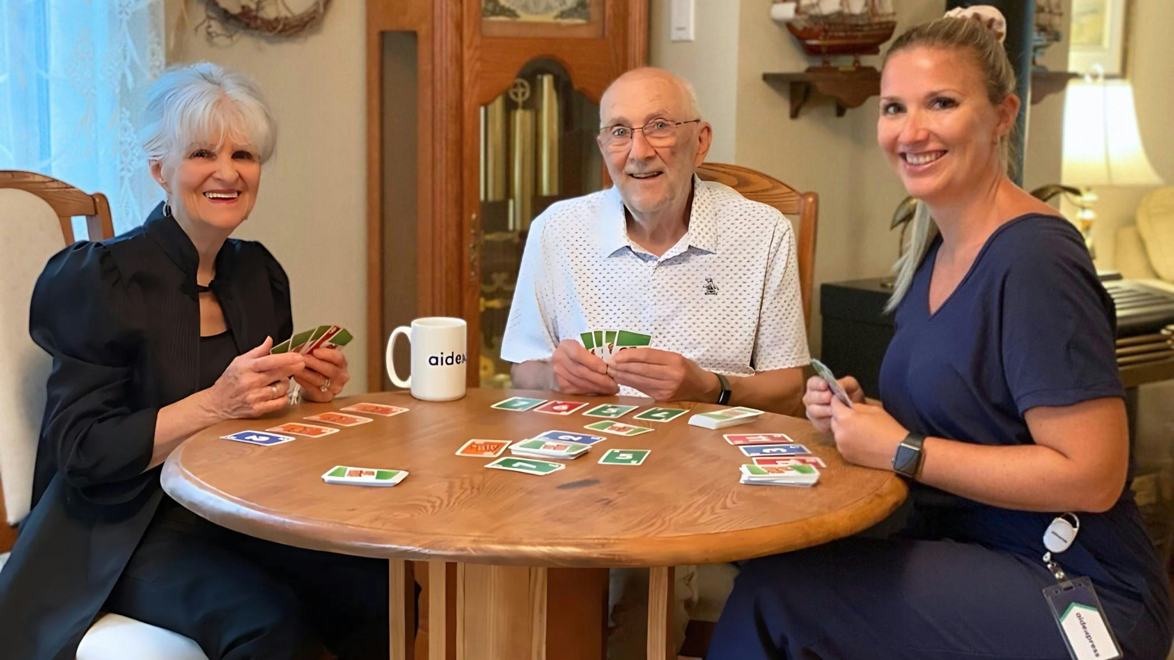 une aidante d'aidexpress qui joue aux cartes avec un couple de personnes âgées
