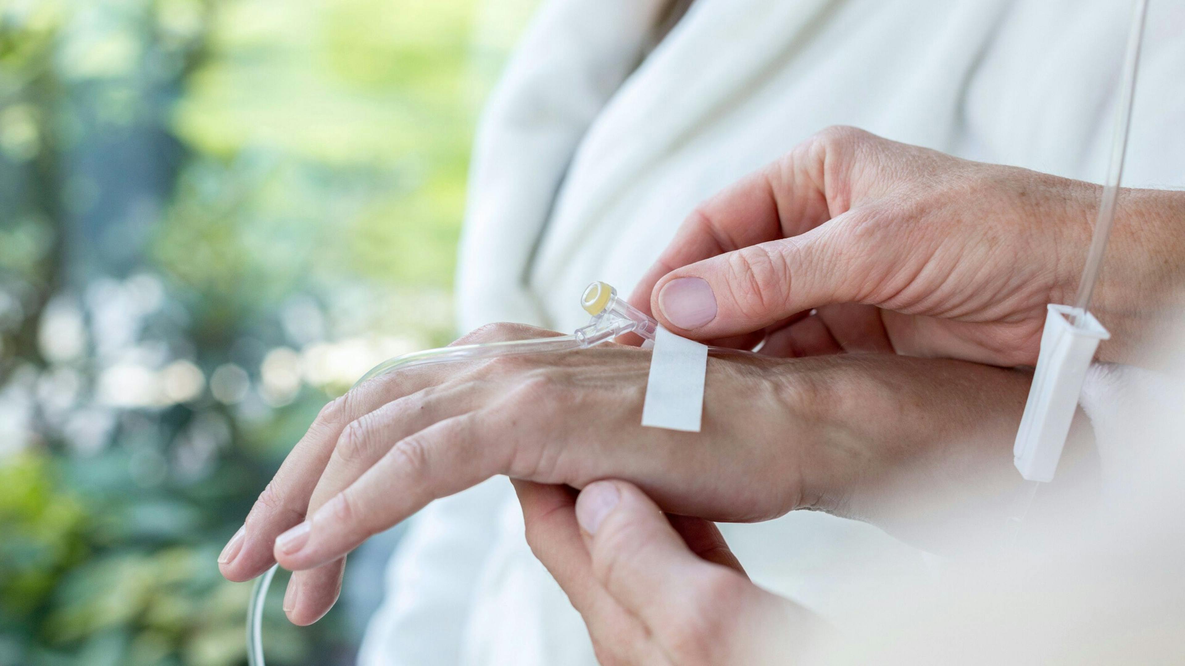 Une préposée en soins à domicile change le pansement sur un cathéter d’une personne âgée, illustrant la surveillance des dispositifs médicaux et la prévention des infections à domicile.