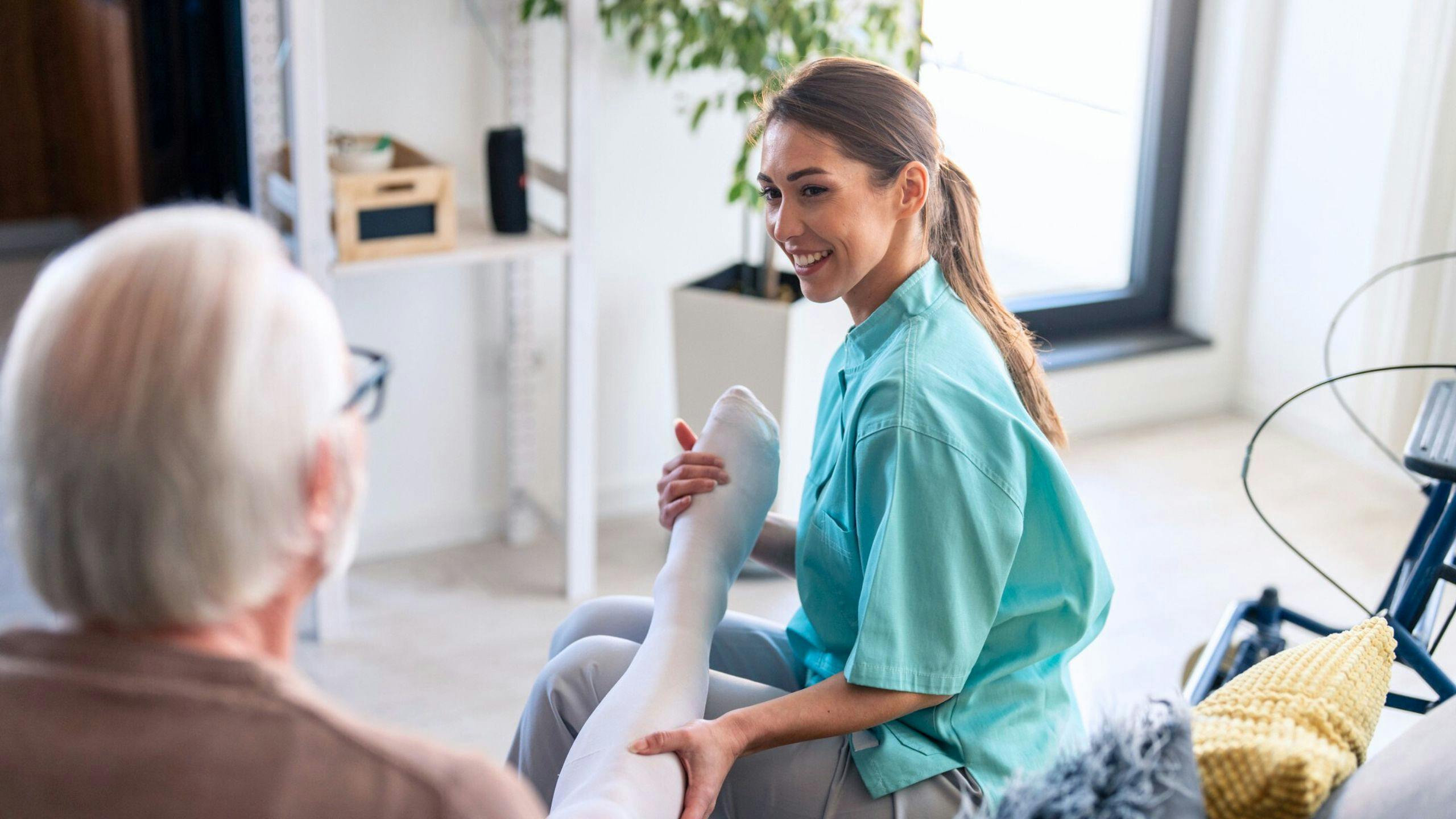 Préposée Aidexpress aidant une personne âgée à mettre ses bas de compression