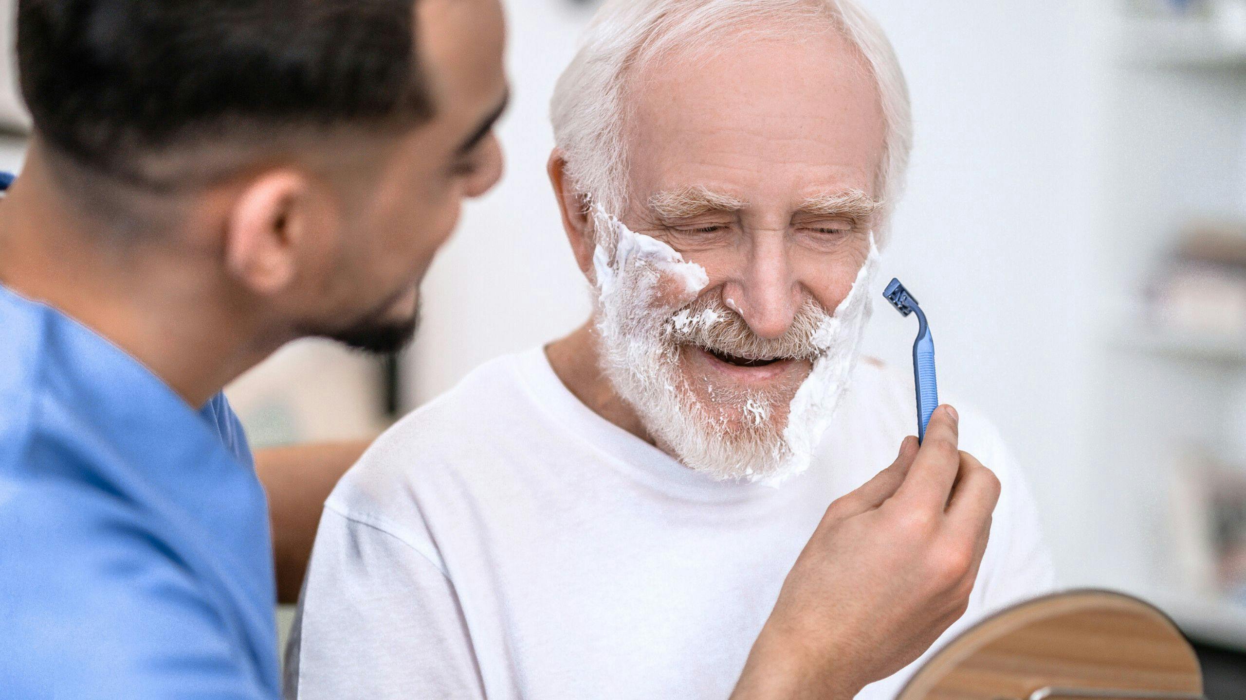 Préposée aidant un homme âgé à se raser la barbe, dans son domicile