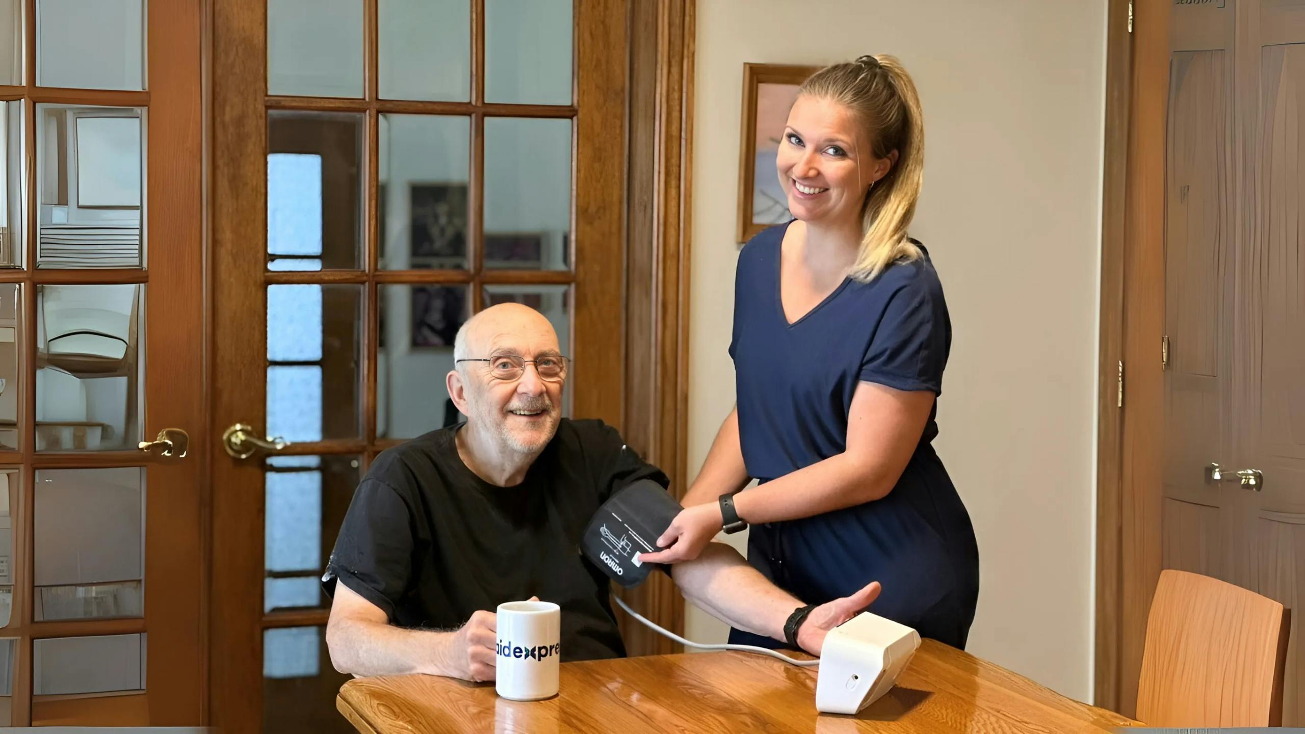 Une préposée en soins à domicile prend la tension artérielle d’un homme âgé, illustrant le suivi médical, la prévention et l’accompagnement sécuritaire des aînés.