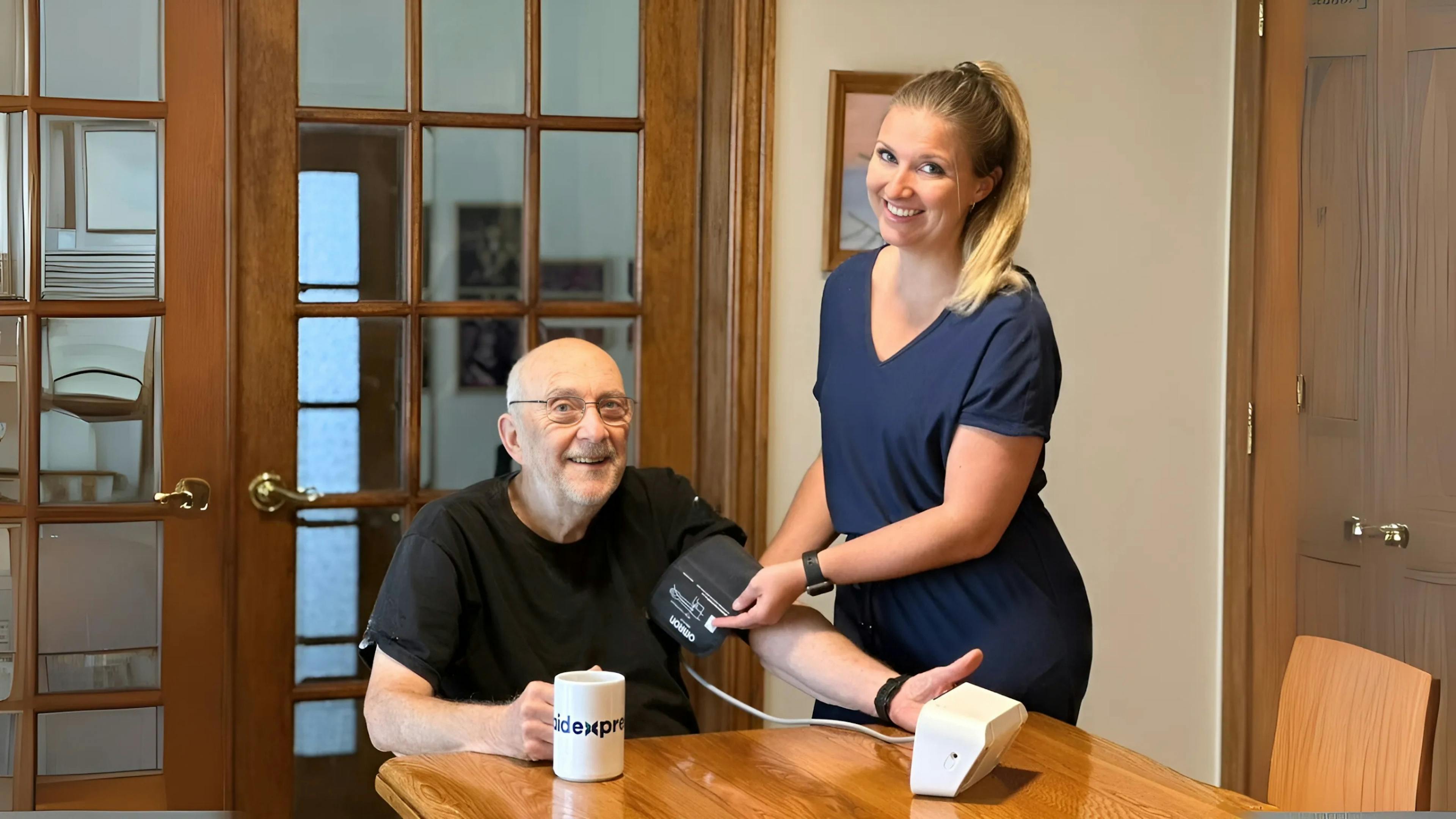 Une préposée en soins à domicile prend la tension artérielle d’un homme âgé, illustrant le suivi médical, la prévention et l’accompagnement sécuritaire des aînés.