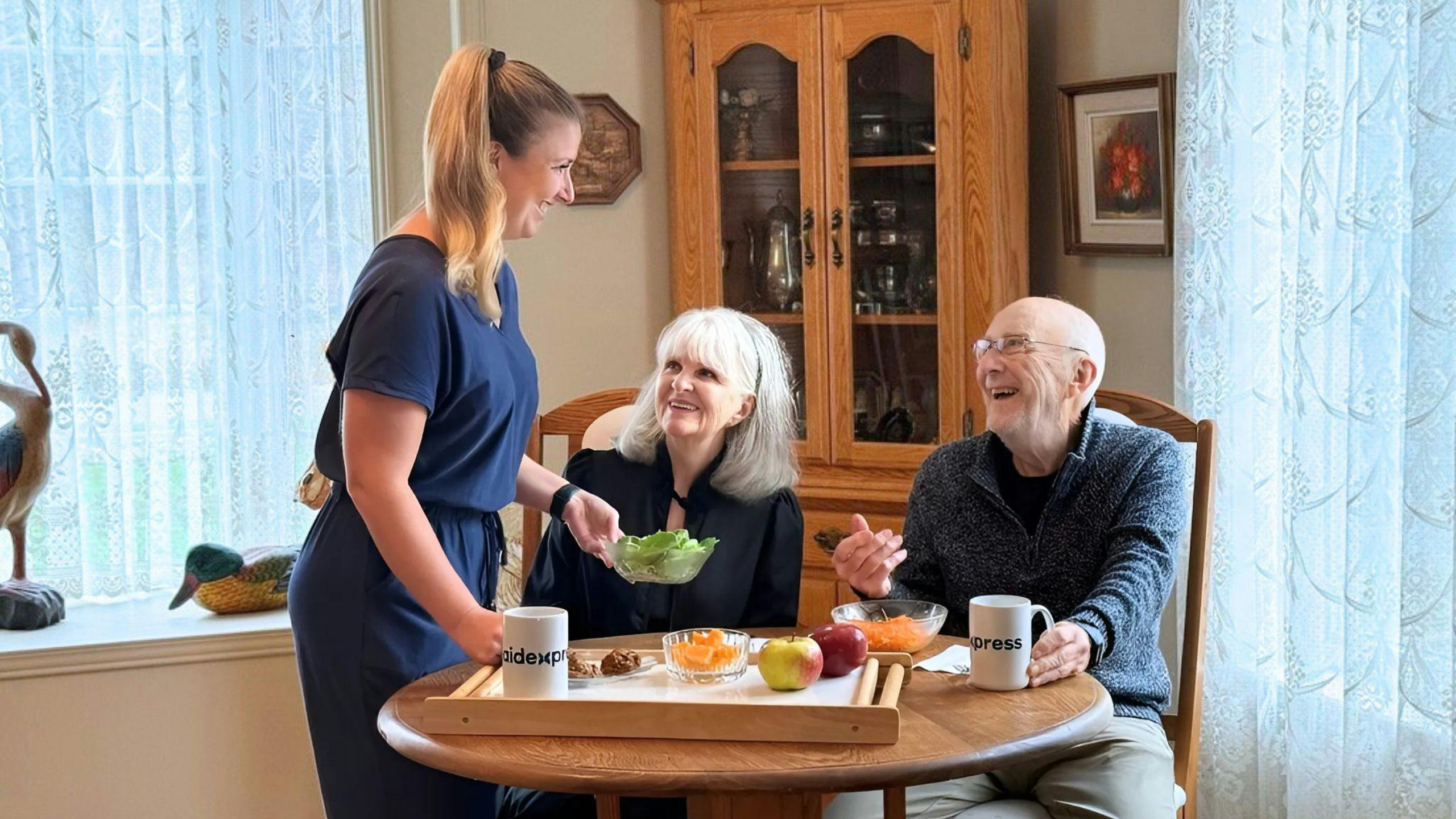 Aidante Aidexpress servant un repas à un couple âgé dans leur maison, illustration des services d’aide à domicile pour confort, autonomie et bien-être.