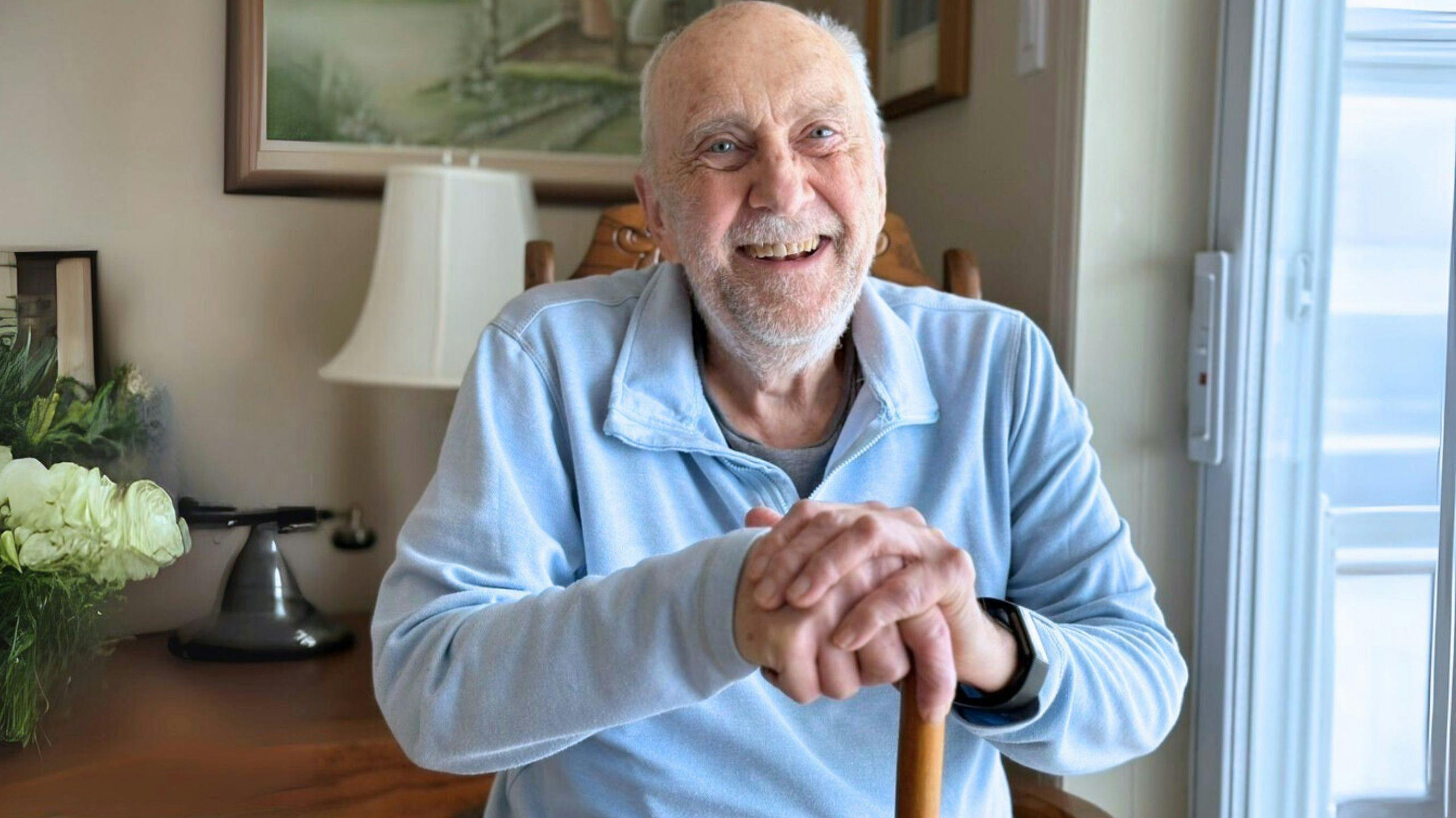 Man with a cane, relaxed and smiling at home, receiving Aidexpress care and support services for people with reduced mobility, respectful, compassionate, and personalized.
