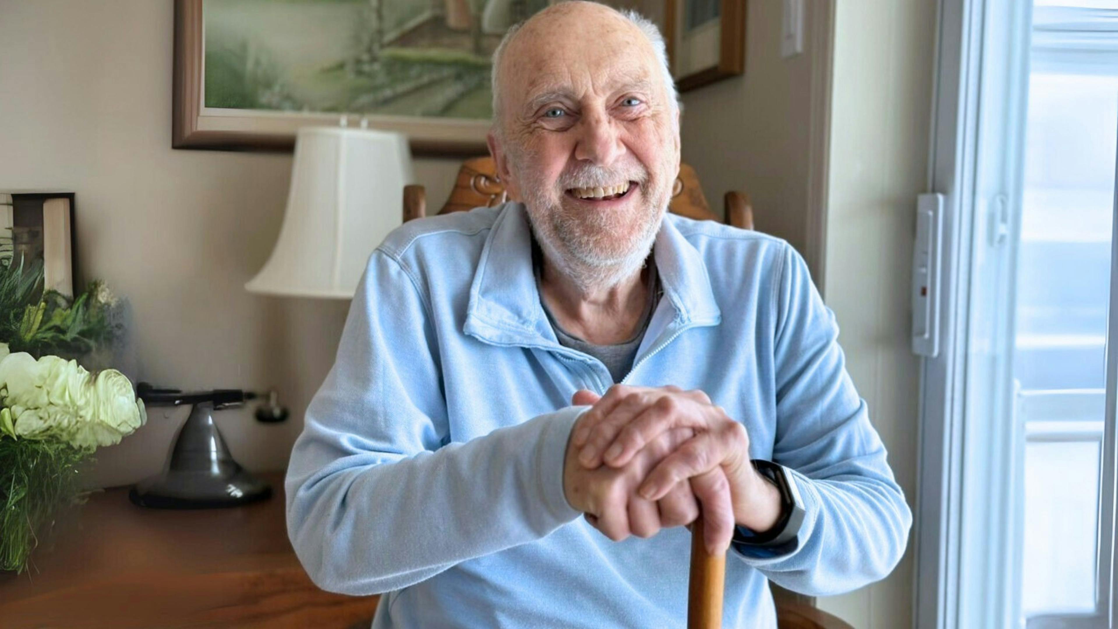 Man with a cane, relaxed and smiling at home, receiving Aidexpress care and support services for people with reduced mobility, respectful, compassionate, and personalized.