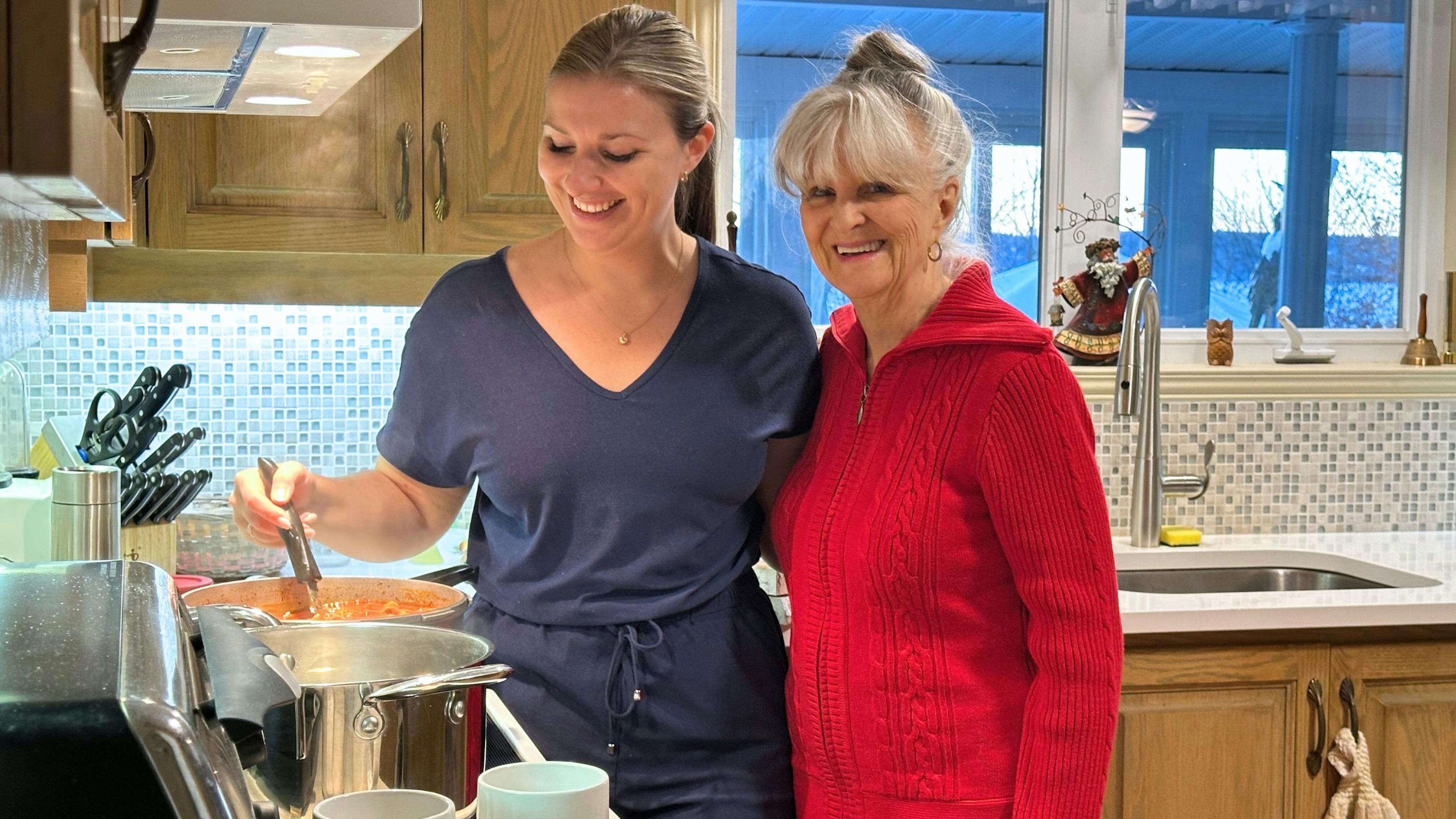 Une aidante souriante d'Aidexpress qui prépare un repas à une personne âgée à son domicile