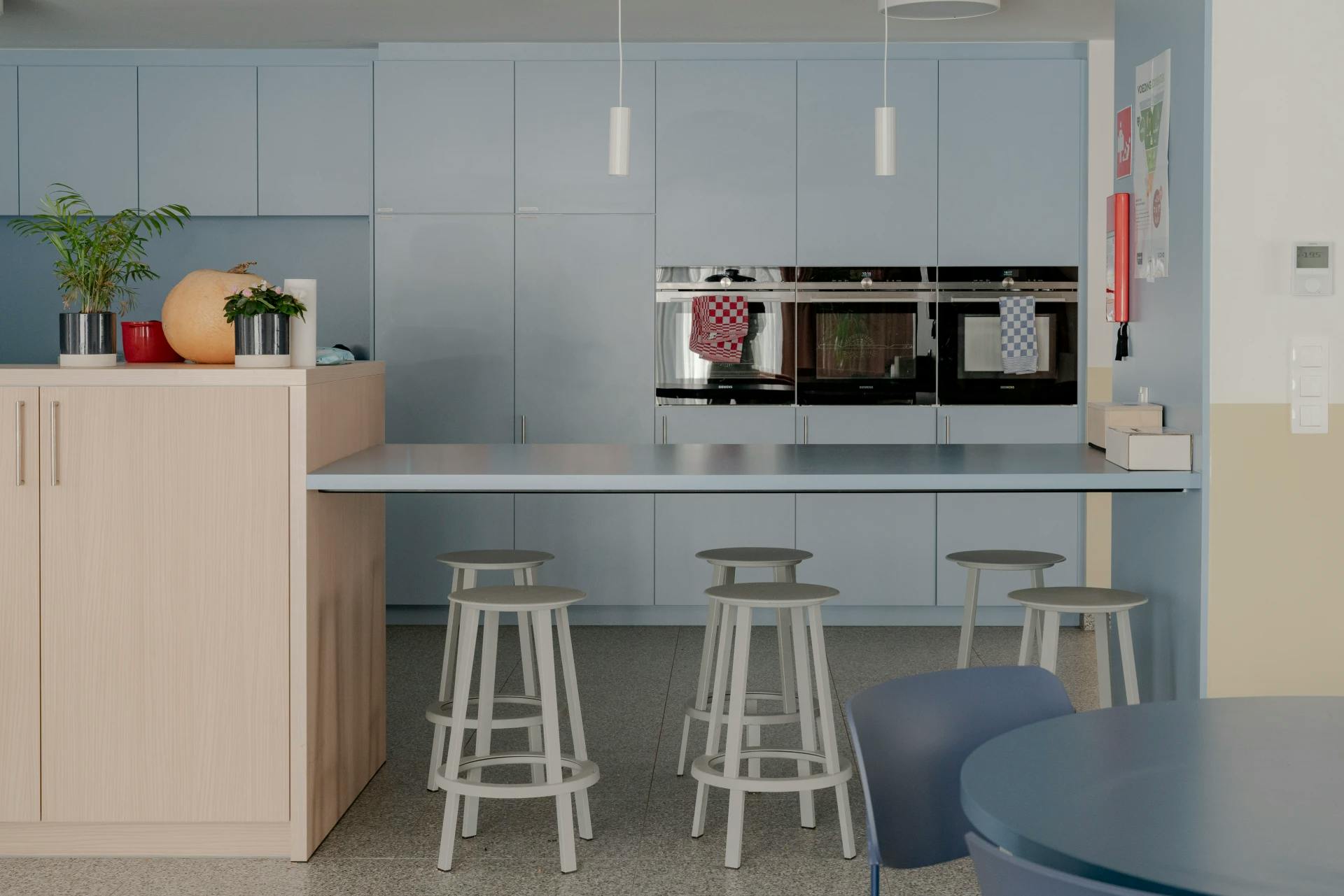Lichtblauwe keuken met eiland en krukken, voorzien van moderne apparatuur en decoratie.