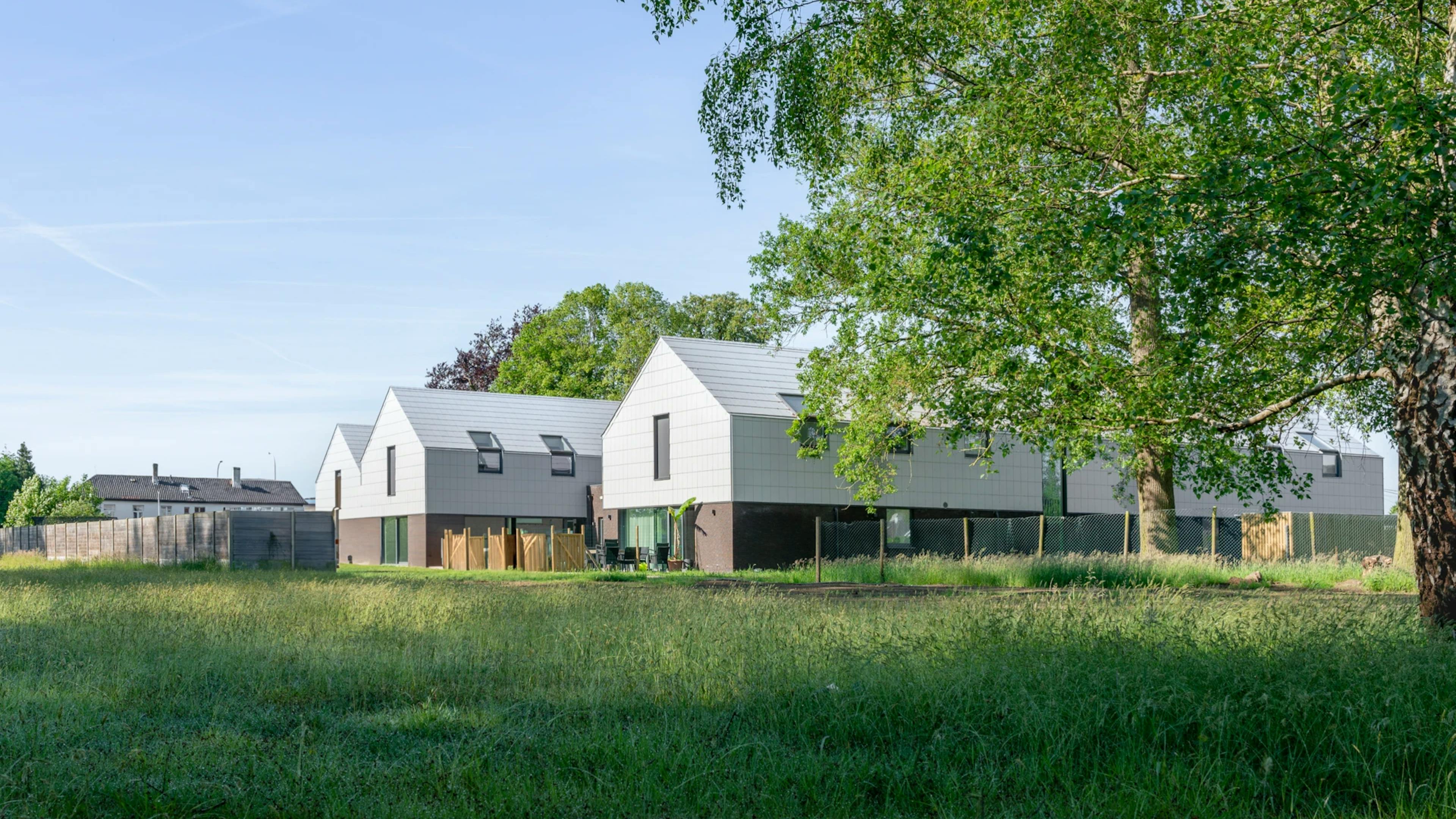 Modern, wit gebouw omgeven door grasvelden en bomen, onder een blauwe lucht.