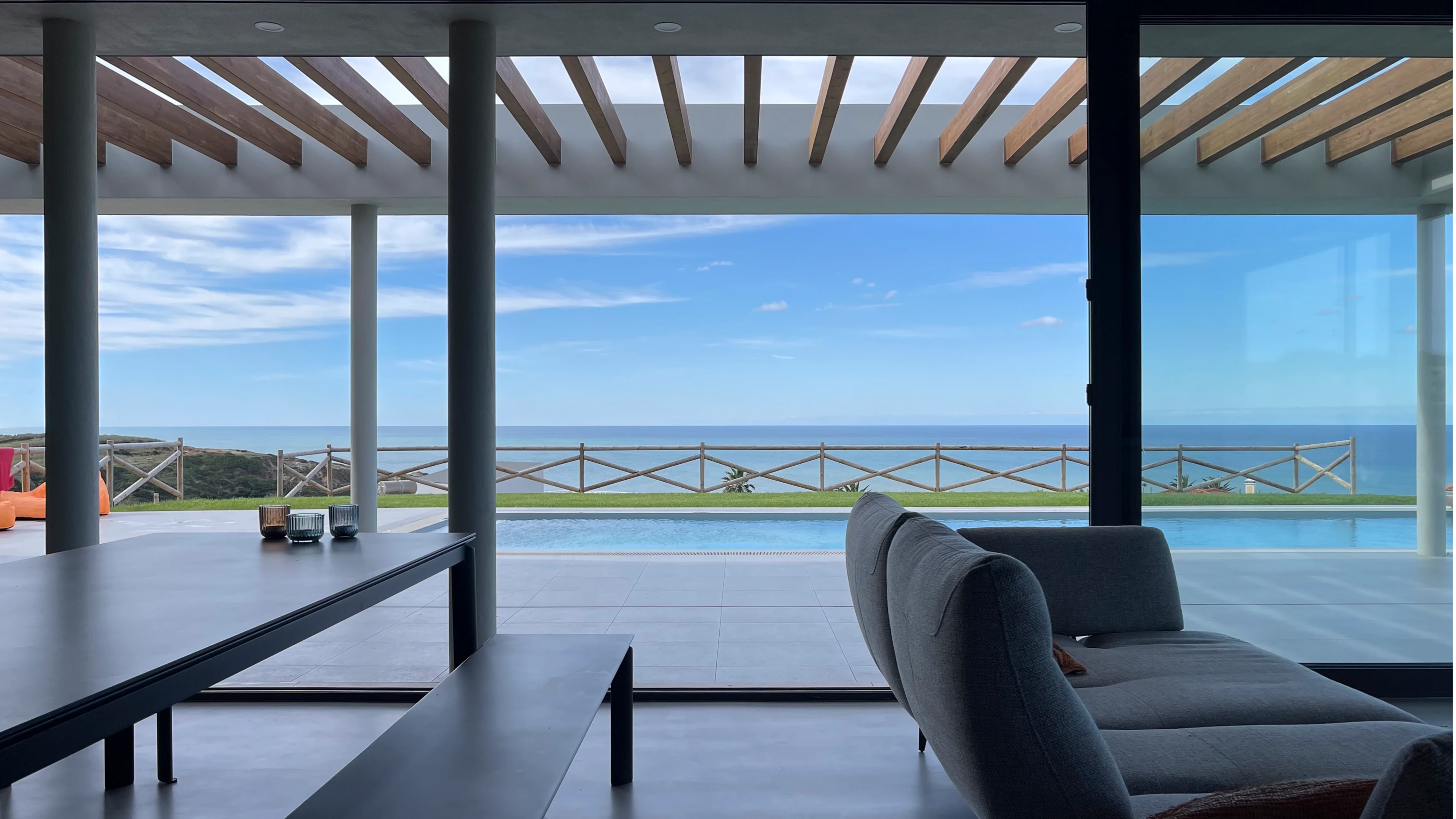 Open terras met glazen wanden, houten pergola en uitzicht op het zwembad en de oceaan.