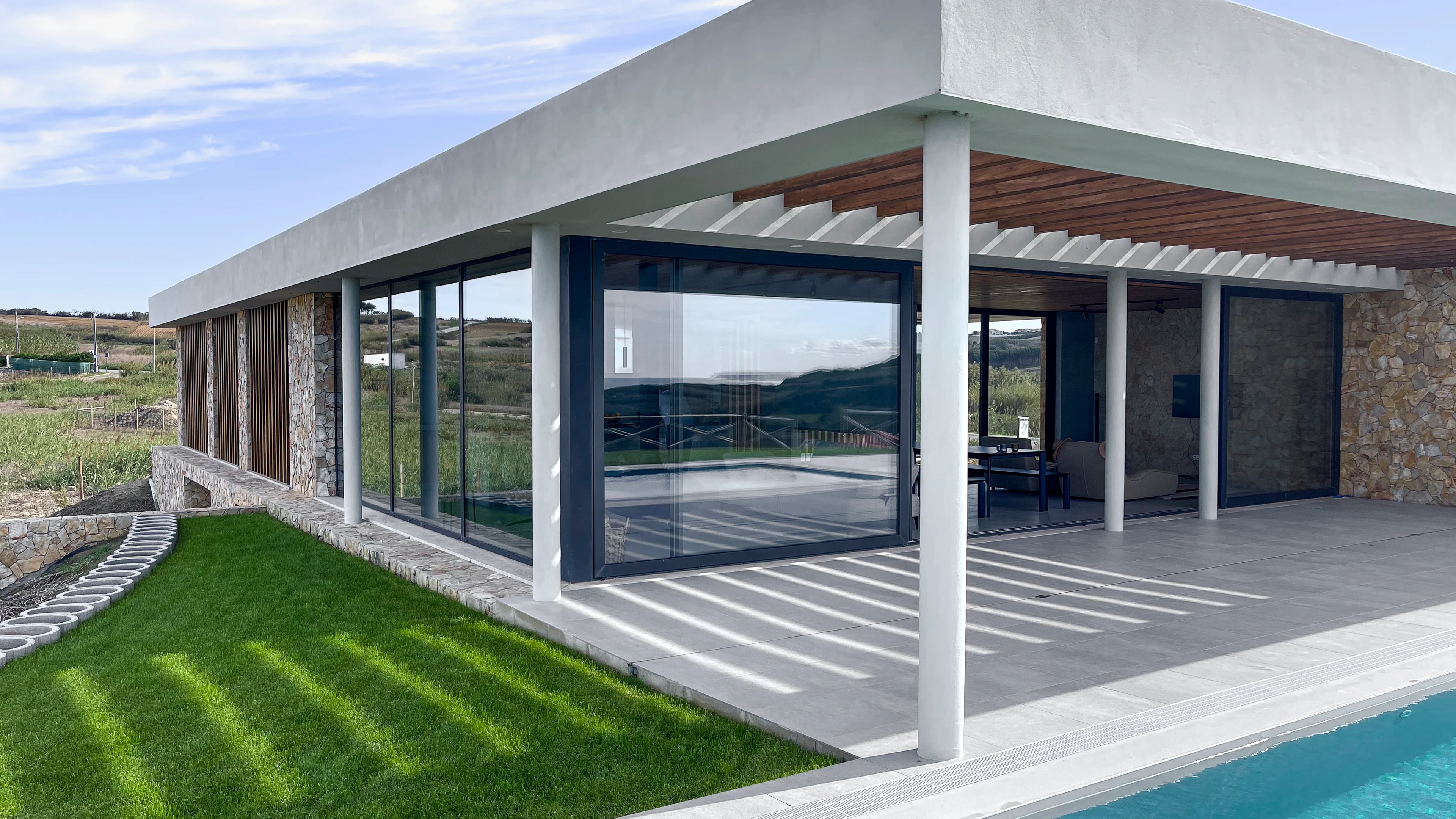 Exterieur van een modern huis met wit gestucte muren, glazen wanden en een zwembad met omliggend grasveld.