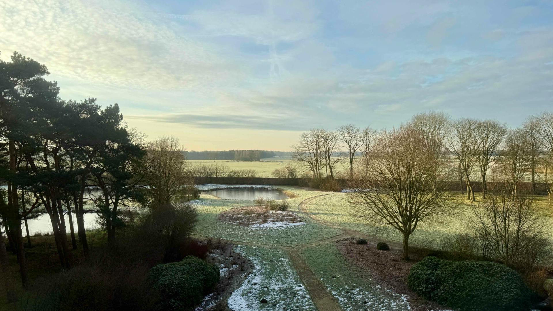 Winterlandschap met vijvers, bomen en besneeuwde velden bij zonsopgang.