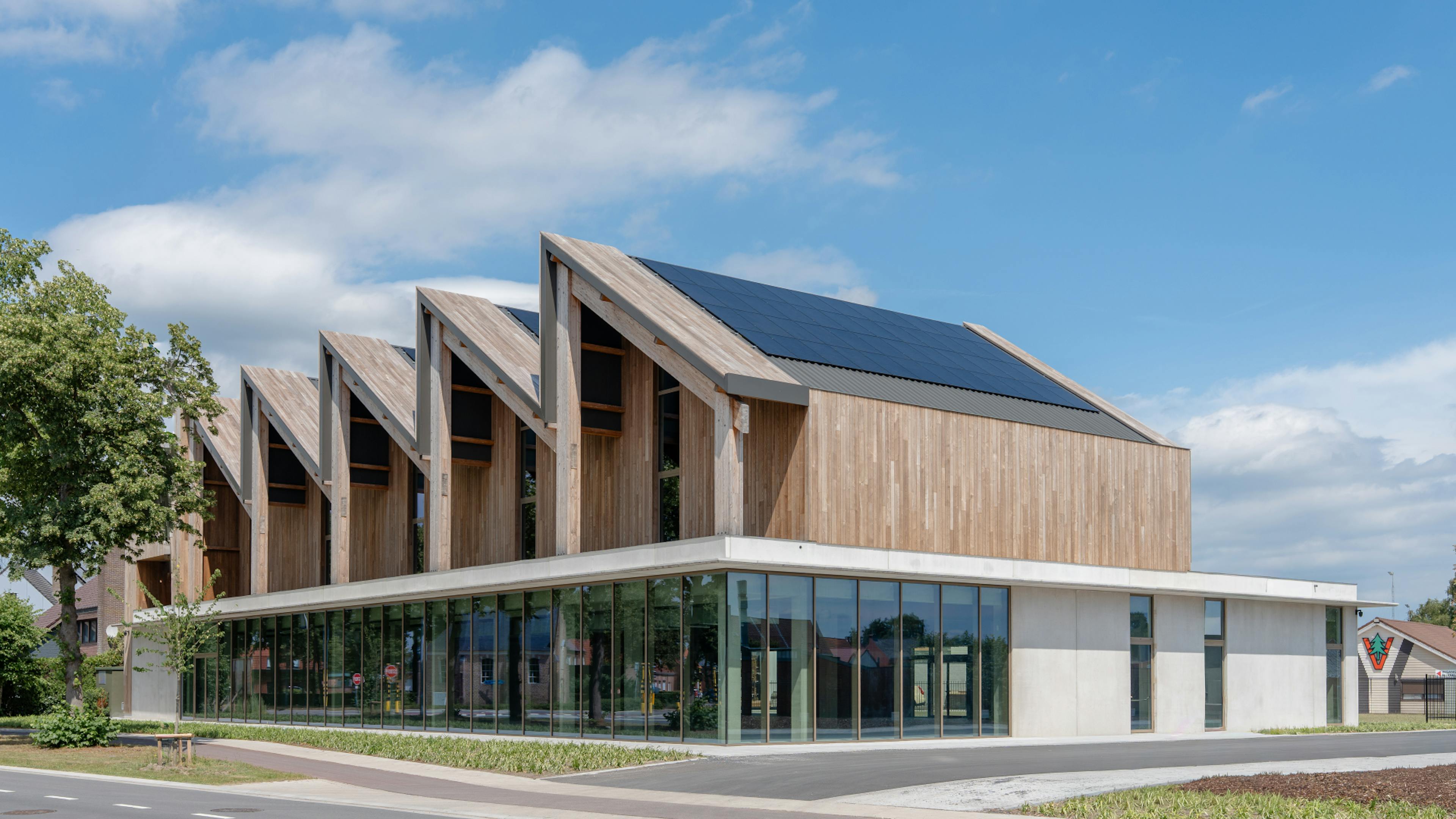 Gebouw met opvallende zaagtanddaken en glazen benedenverdieping aan een kruispunt.