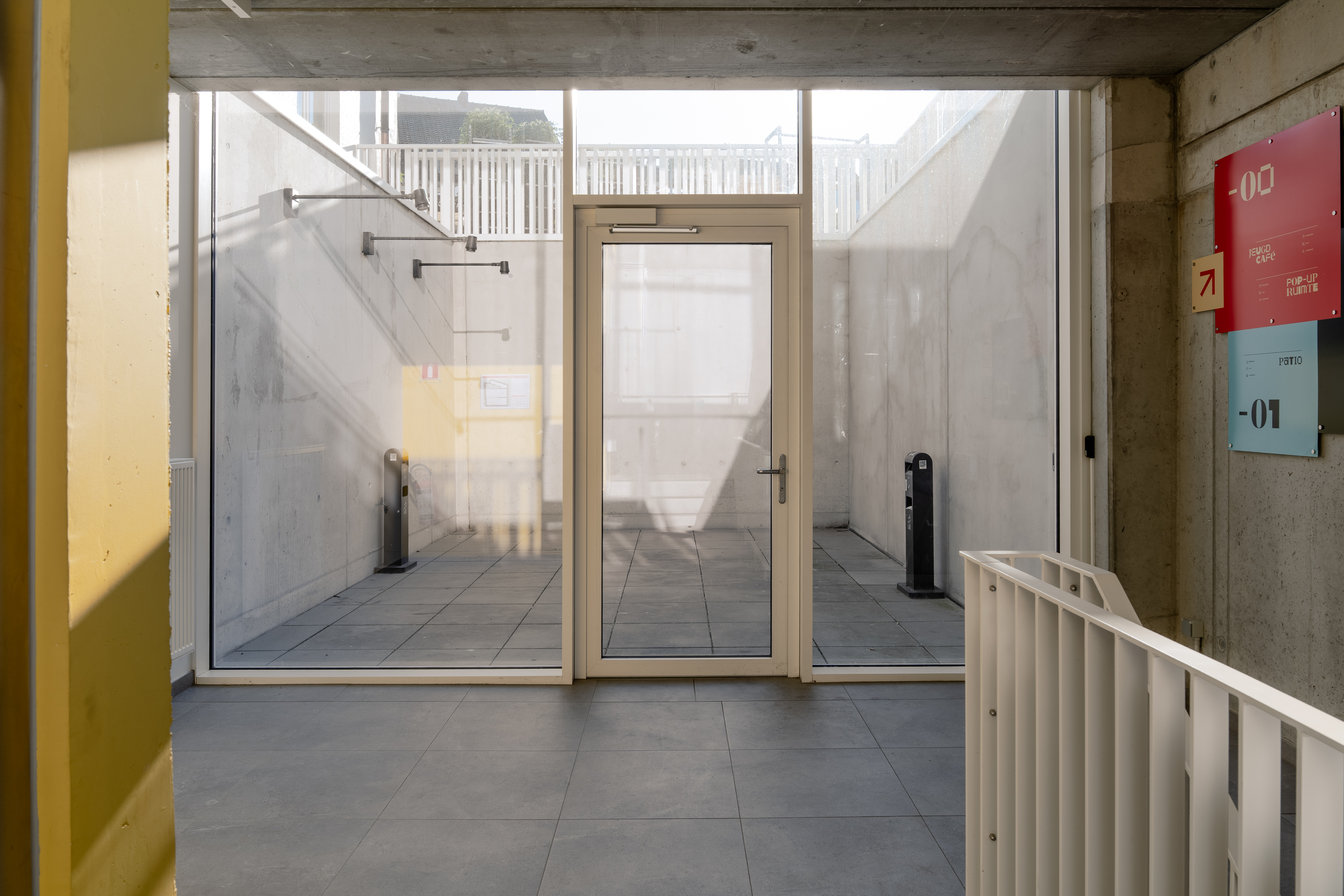 Ingang met glazen deur en zicht op ommuurde buitenruimte.