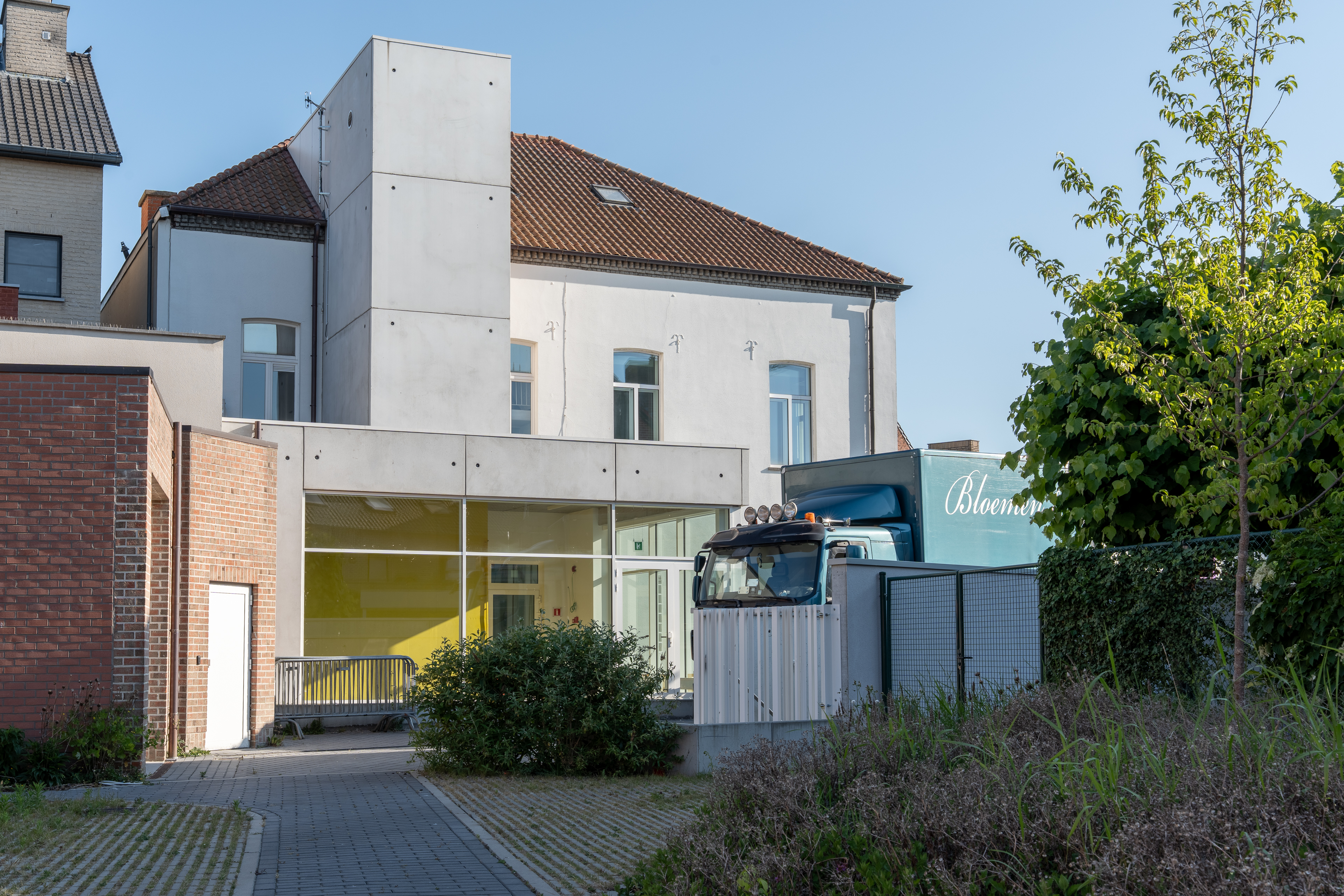 Achterkant van gebouw met witte gevel, grote ramen en geparkeerde vrachtwagen.