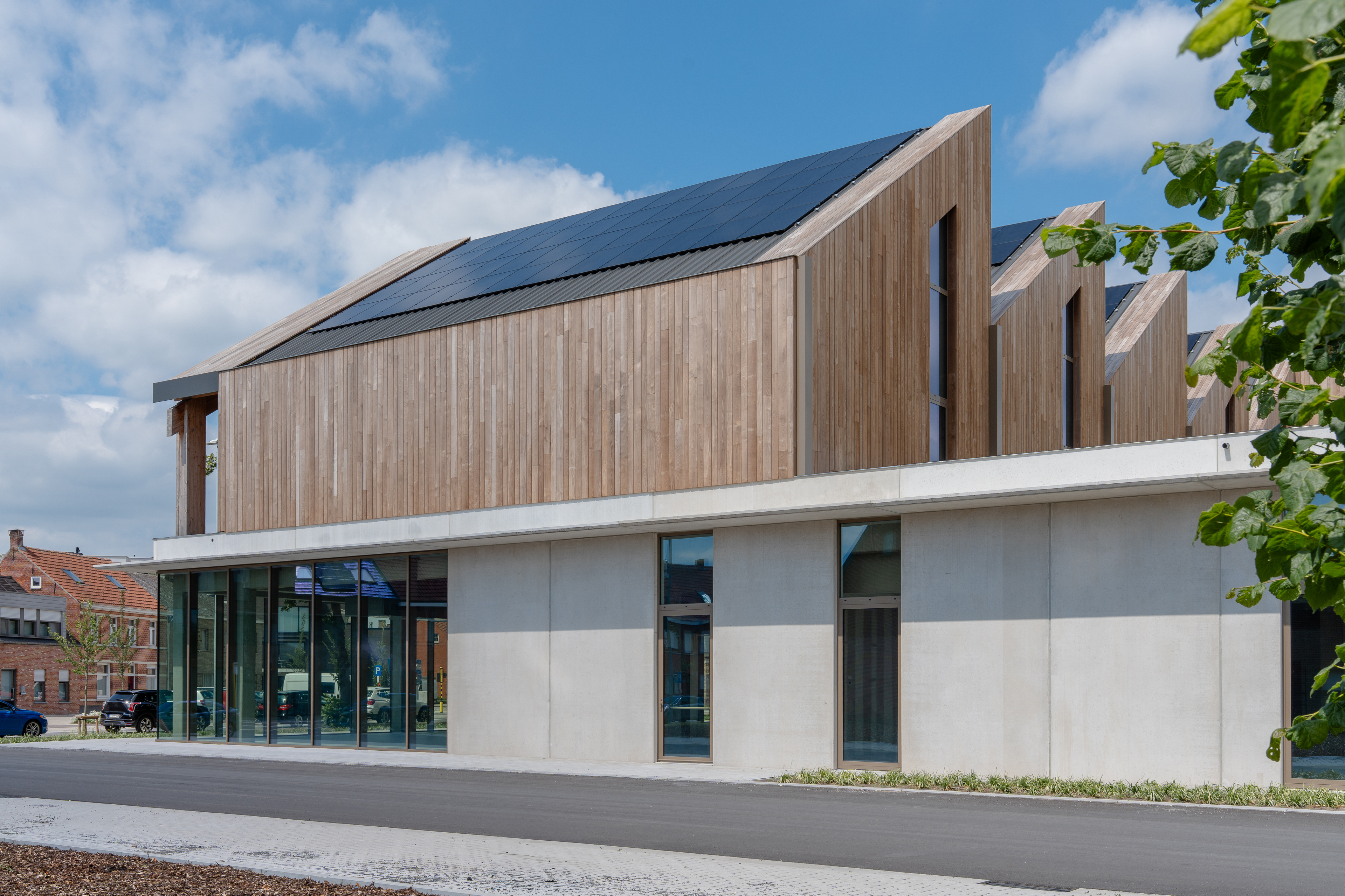 Modern gebouw met houten gevels en zonnepanelen op een schuindak onder blauwe lucht.