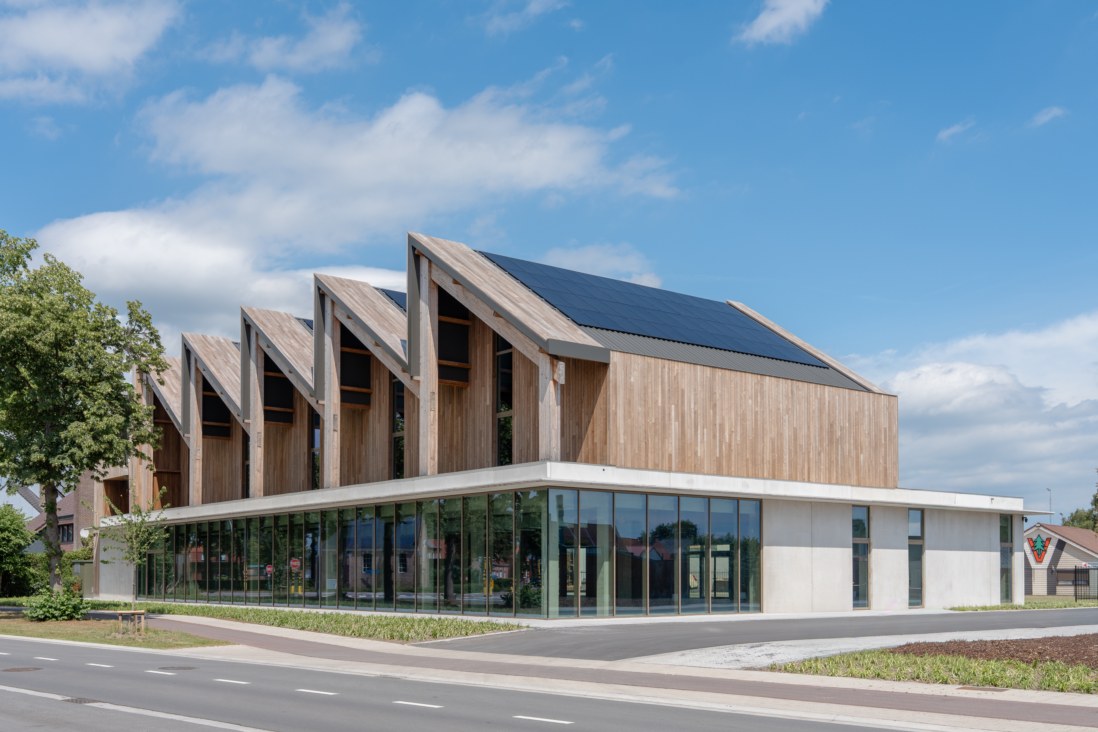 Gebouw met opvallende zaagtanddaken en glazen benedenverdieping aan een kruispunt.