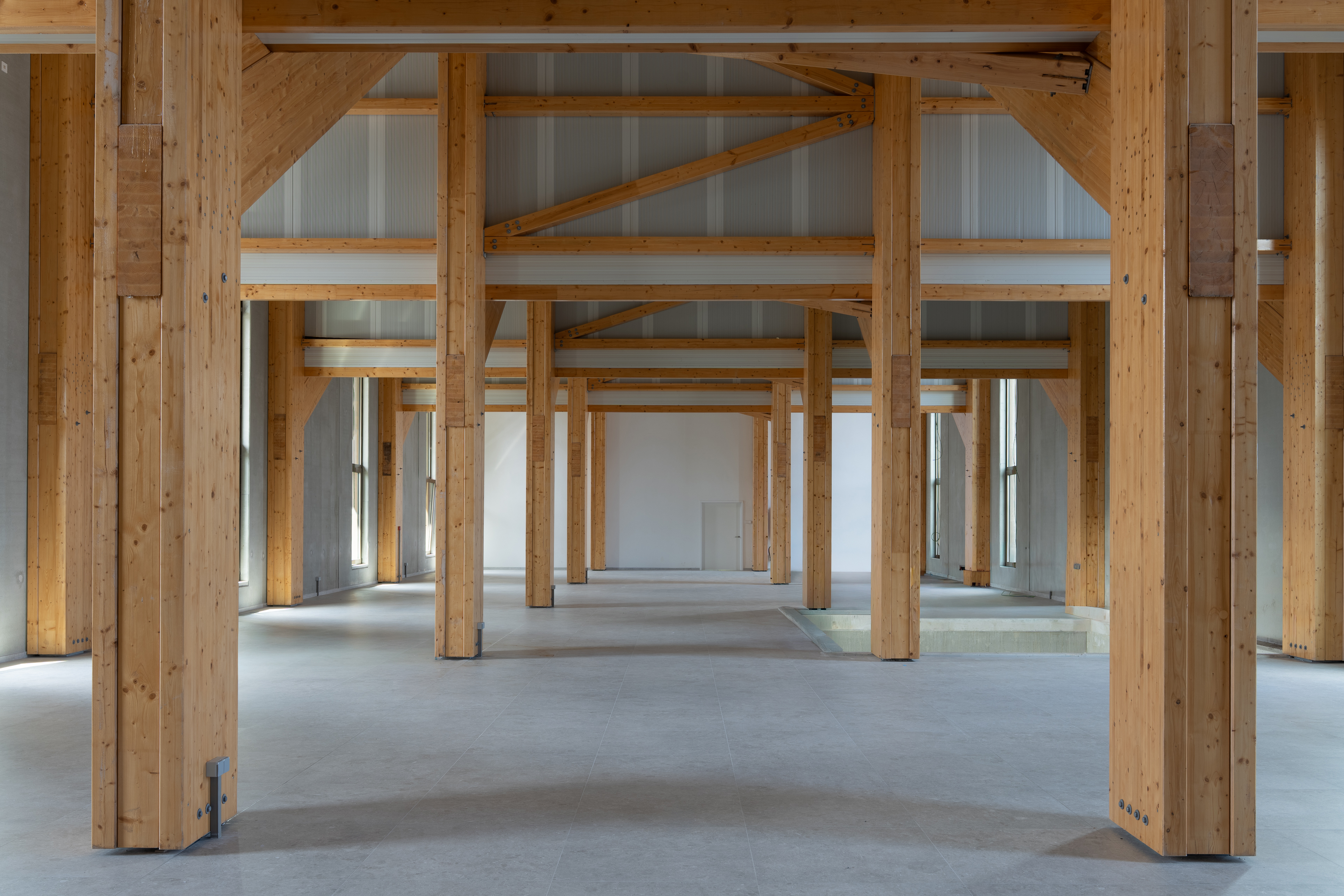 Interieur met houten balkenstructuur, betonnen vloer en hoge plafonds met daglicht.