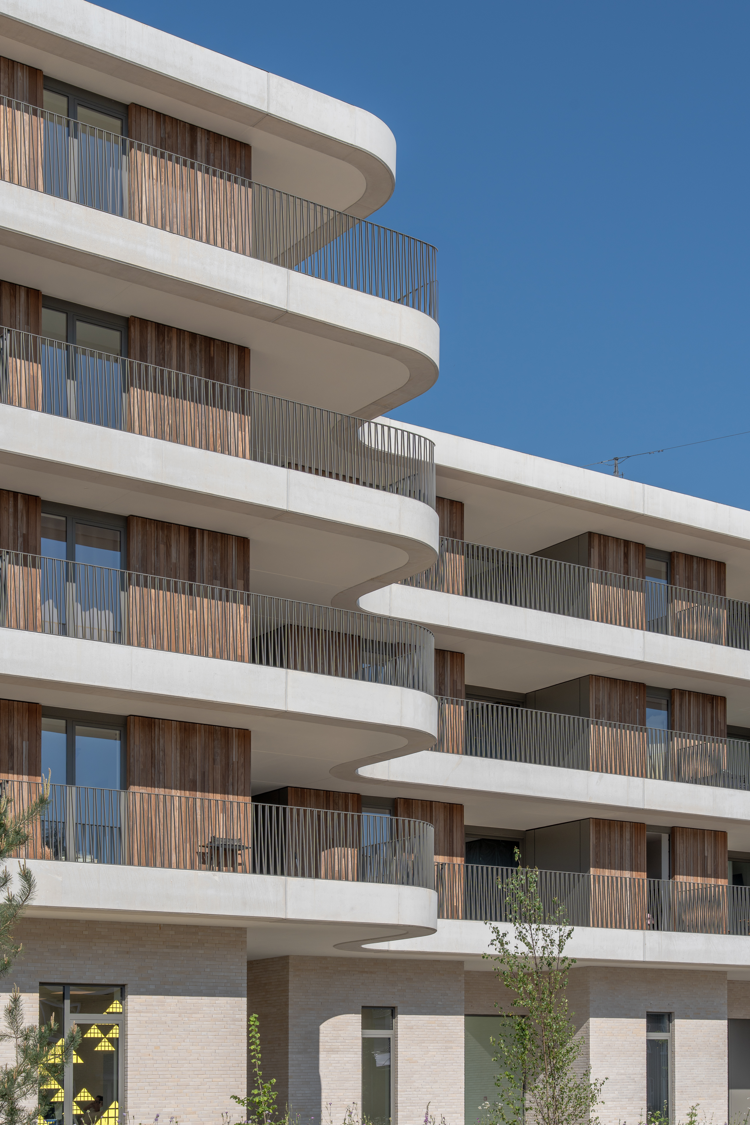 Close-up van gebogen balkons met houten panelen en metalen hekwerk tegen blauwe lucht.