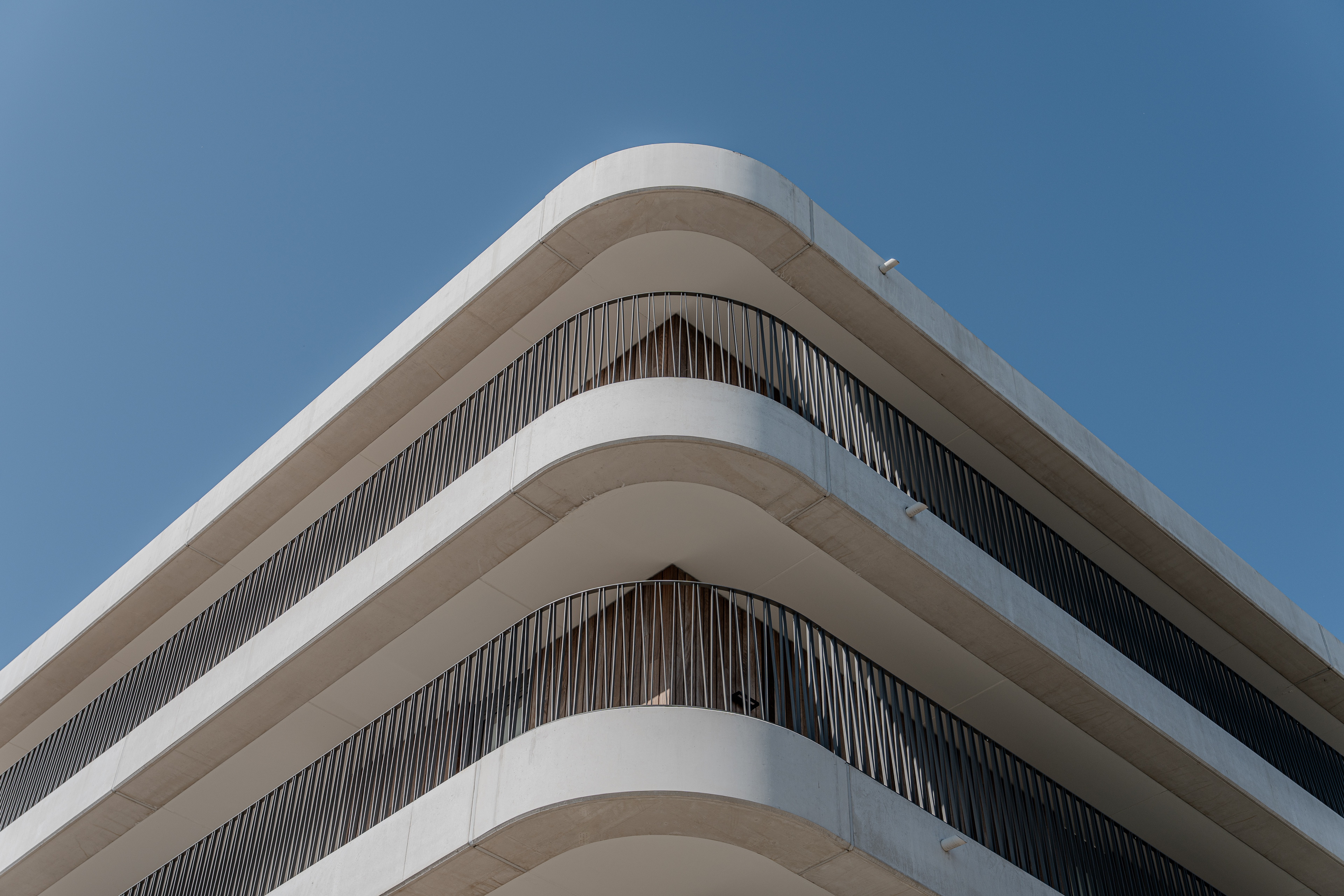 Strakke hoek van gebouw met ronde witte balkons en zwart hekwerk tegen blauwe lucht.