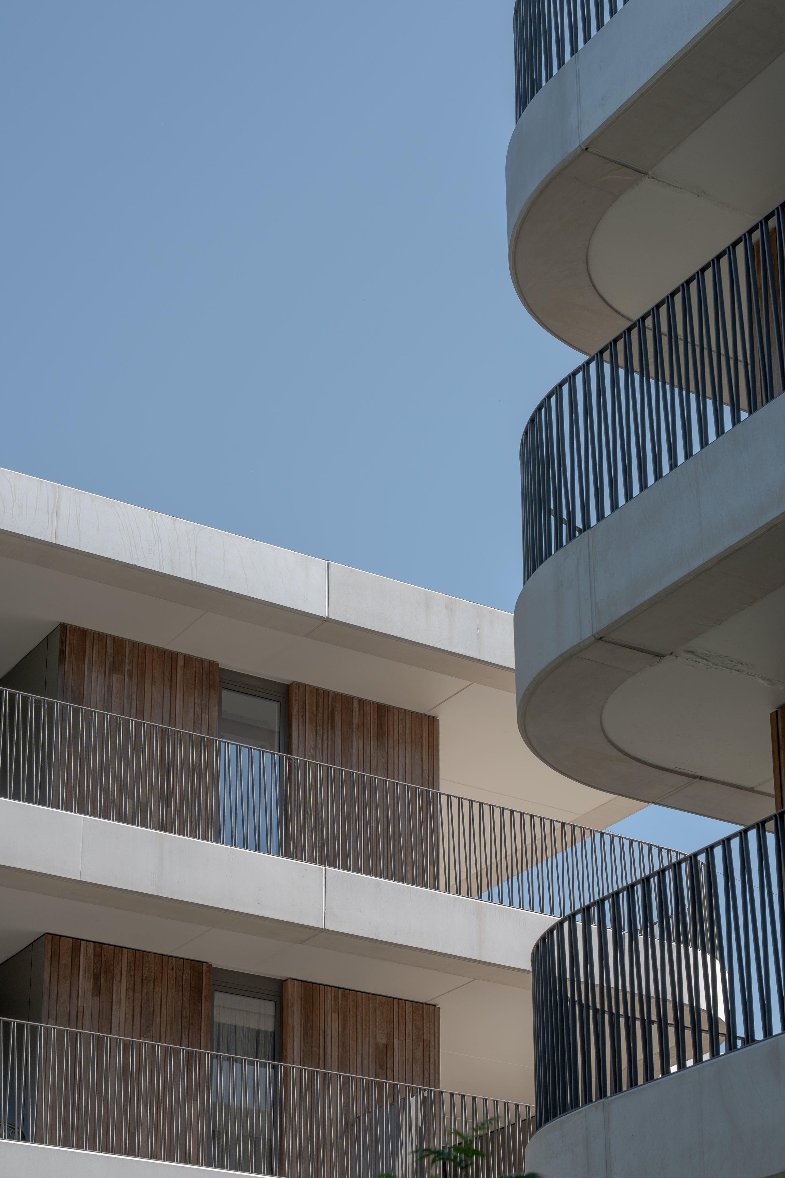 Detail van twee gebouwen met afgeronde balkons en houten gevels tegen blauwe lucht.