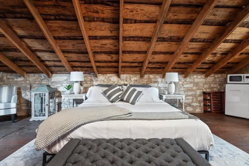 Bedroom in a Bach Bros Properties rental with a king bed, exposed wood ceiling beams and limestone walls