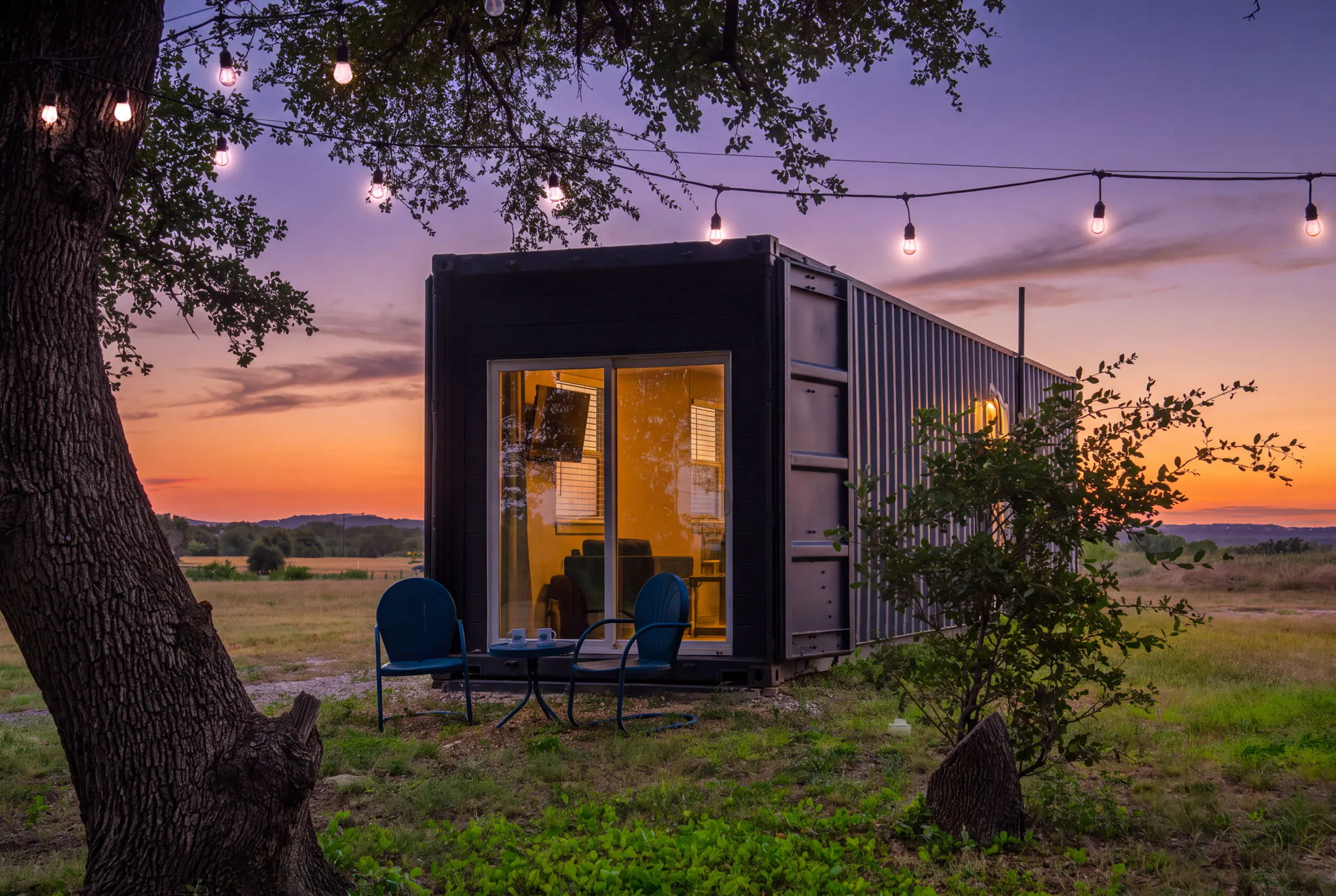 Shipping container guest house managed by Bach Bros Properties at sunset, with string lights and two patio chairs