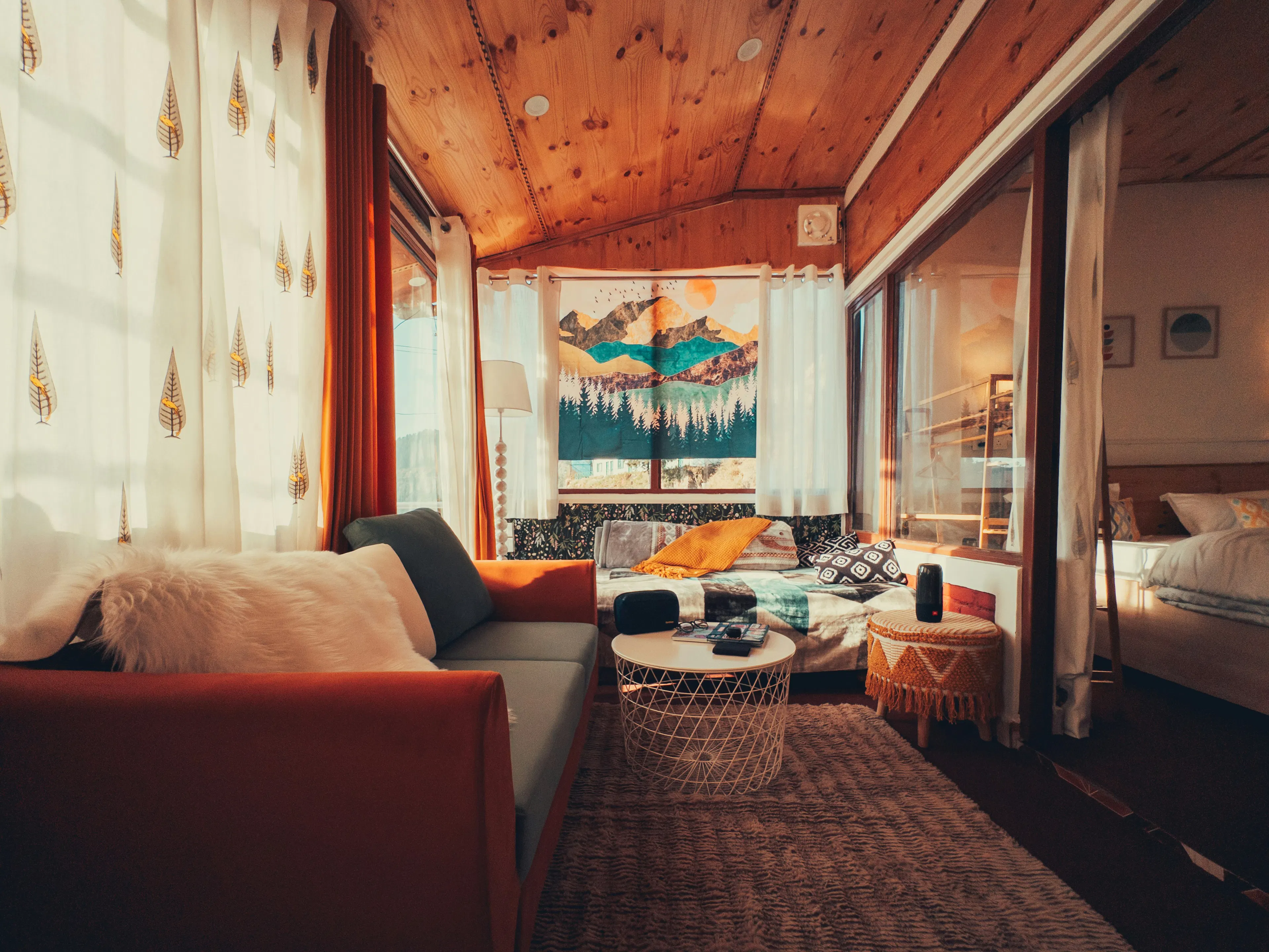 A cozy, sunlit living area with a terracotta couch, wooden ceilings, and a mountain tapestry
