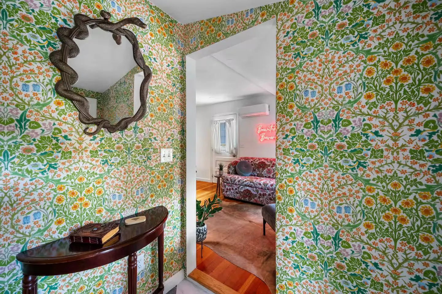Entry of the Witchy Private Cottage in Beverly, Massachusetts, with bold floral wallpaper and a serpent-framed mirror