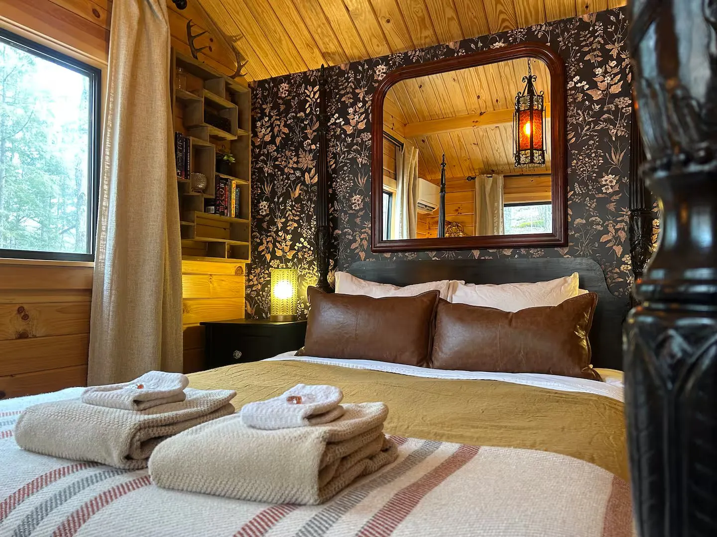 Bedroom at the Alchemist’s Cabin in Duxbury, Vermont, with dark floral wallpaper, an antique mirror and a hanging lantern